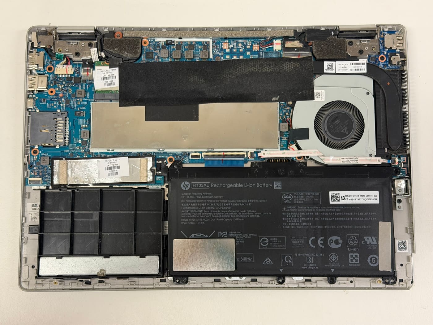 Inside an HP laptop on our Perth bench — motherboard, cooling fan and HT03XL battery